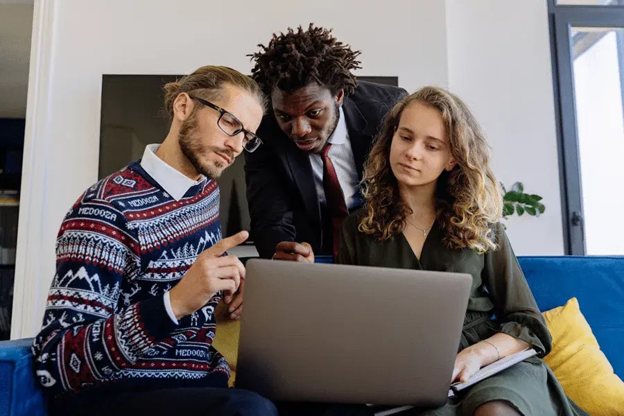 Three people collaborating on how to set up a family office, viewing a laptop for a comprehensive guide.