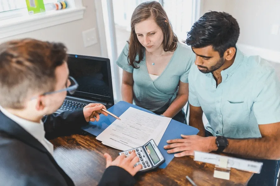 Three people discuss international estate planning tools, reviewing documents and using a calculator in an office.