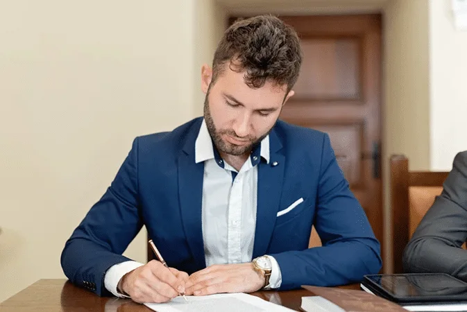 A man in a suit signs documents at a desk, symbolizing discretionary trusts in international estate planning benefits.