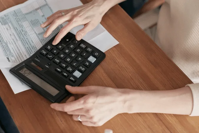 Hands using a calculator on financial documents, representing tax planning in international estate management to reduce liabilities.